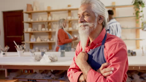 Happy-biracial-potter-with-long-beard-sitting-and-smiling-in-pottery-studio,-slow-motion