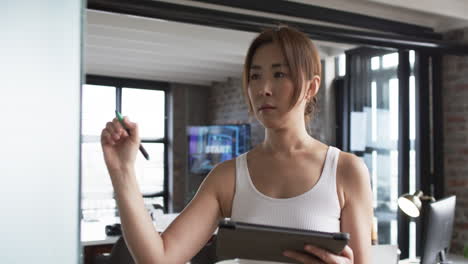 Mujer-De-Negocios-Asiática-Con-Camiseta-Blanca-Sostiene-Una-Tableta-Y-Un-Lápiz-En-Un-Ambiente-De-Oficina