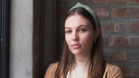 Young-Caucasian-businesswoman-with-brown-hair-and-headband-poses-near-a-window