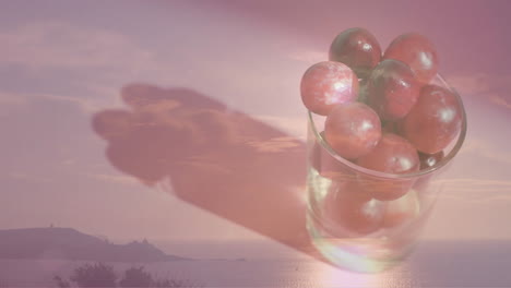 Composition-of-glass-of-red-grapes-over-landscape-background
