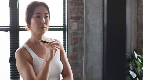 Asian-businesswoman-in-white-tank-top-holds-a-pen,-looking-pensive,-with-copy-space