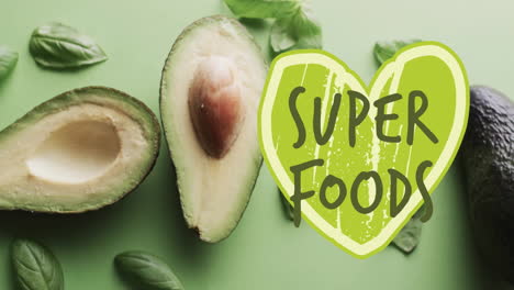 Animation-of-super-foods-text-on-green-heart-over-avocado-on-green-background
