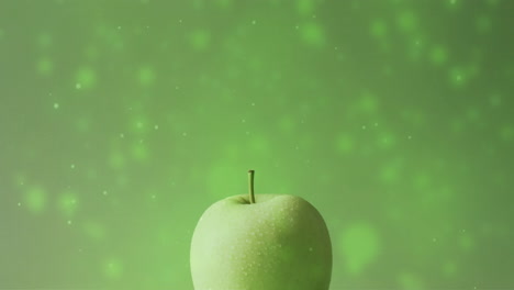 Composition-of-green-apple-over-spots-of-light-on-green-background