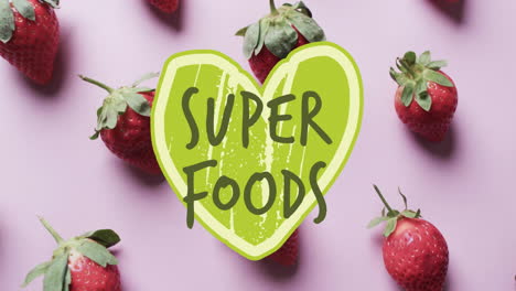 Animation-of-super-foods-text-over-halved-strawberries-on-pink-background