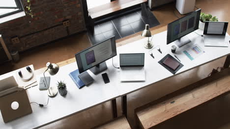 Multiple-workstations-with-laptops,-smartphones,-and-desk-lamps-in-a-business-setting