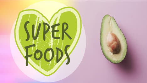 Animation-of-super-foods-text-on-green-heart-over-halved-avocado-on-pink-background