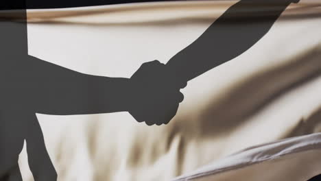 Animation-of-silhouettes-of-people-shaking-hands-and-floating-cloth-on-black-background