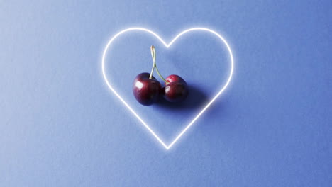 Composition-of-cherries-and-neon-heart-shape-over-blue-background