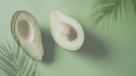 Animation-Von-Palmenblättern-über-Halbierter-Avocado-Auf-Grünem-Hintergrund