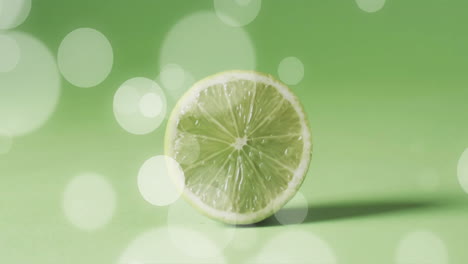 Composition-of-halved-lime-over-white-spots-of-light-on-green-background
