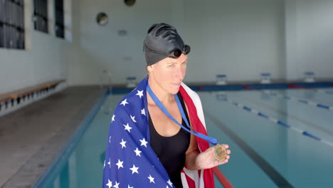 An-American-flag-draped-Caucasian-female-swimmer-athlete-stands-proudly-at-a-poolside