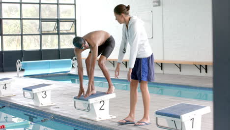 Swimming-coach-instructs-a-young-biracial-male-athlete-swimmer-at-the-poolside