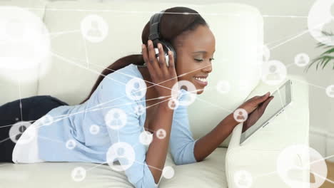 Animation-of-network-of-connections-with-icons-over-african-american-woman-using-tablet