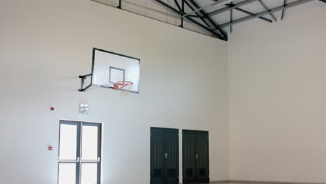 An-indoor-basketball-hoop-is-mounted-on-a-white-wall-in-a-gymnasium