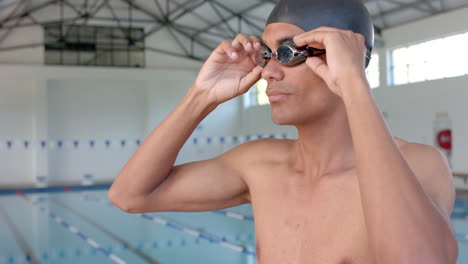Young-biracial-man-adjusts-his-swimming-goggles-at-the-pool