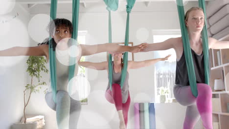 Animation-of-light-spots-over-diverse-female-instructor-and-teenage-girls-practicing-aerial-yoga