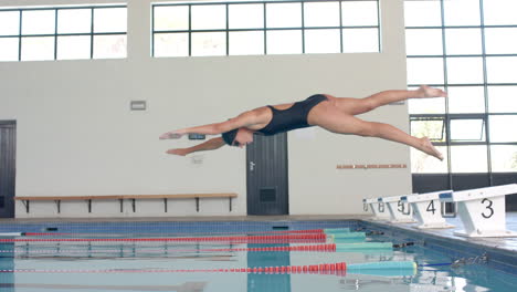 Caucasian-female-swimmer-athlete-executes-a-dive-at-an-indoor-pool