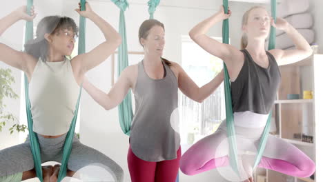 Animation-of-light-spots-over-diverse-female-instructor-and-teenage-girls-practicing-aerial-yoga