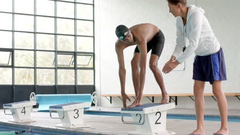 Coach-instructs-a-young-biracial-male-athlete-swimmer-at-the-poolside,-with-copy-space