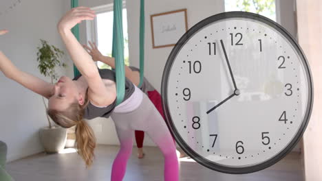 Animation-of-fast-moving-clock-over-caucasian-female-instructor-and-teenage-girl-doing-aerial-yoga