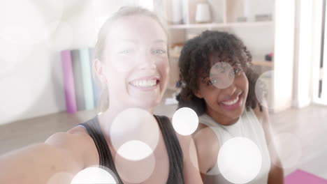 Animation-of-white-light-spots-over-happy-diverse-teenage-girls-taking-selfies-at-yoga-class