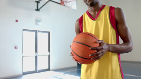 Young-African-American-man-holds-a-basketball-in-a-gym,-with-copy-space