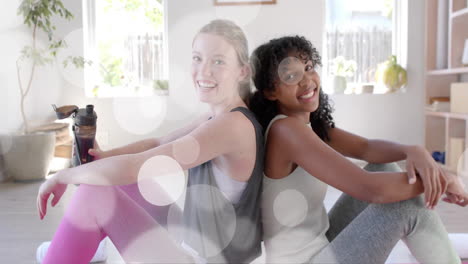 Animation-of-light-spots-over-happy-diverse-teenage-girls-relaxing-after-practicing-yoga