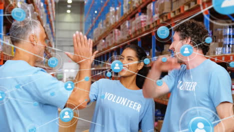 Animation-of-network-of-connections-with-icons-over-diverse-volunteer-high-fiving-in-warehouse