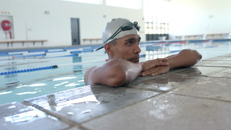 Young-biracial-male-athlete-swimmer-rests-at-the-pool-edge