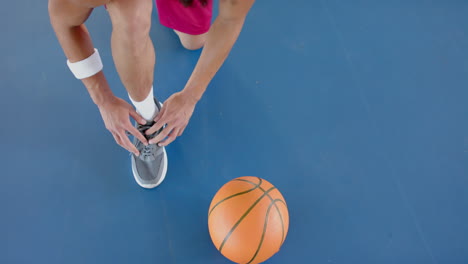 Young-biracial-man-ties-his-shoelaces-on-a-basketball-court