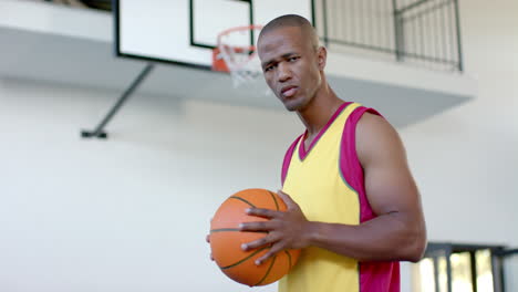 African-American-man-holds-a-basketball,-looking-determined-in-a-gym