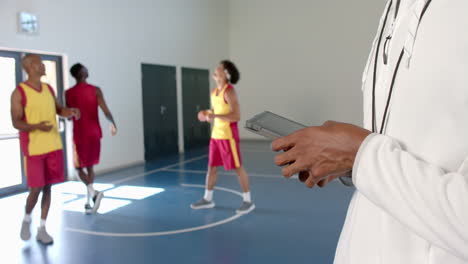 Coach-holding-a-tablet-at-a-basketball-court,-with-copy-space