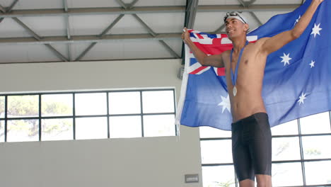 Young-biracial-male-athlete-swimmer-celebrates-victory-at-a-sports-event-with-the-Australian-flag,-w