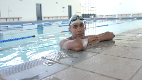 Young-biracial-male-athlete-swimmer-rests-at-the-poolside,-with-copy-space