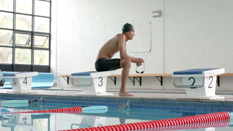 Young-biracial-male-athlete-swimmer-prepares-to-dive-at-an-indoor-pool