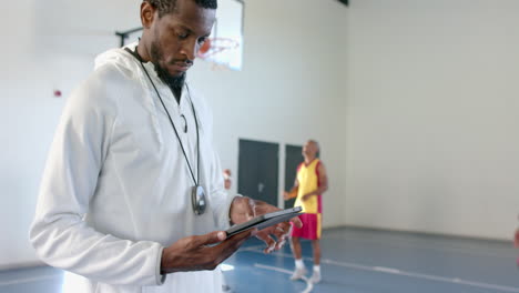 Afroamerikanischer-Trainer-überprüft-Daten-Auf-Einem-Tablet-In-Einer-Sportanlage