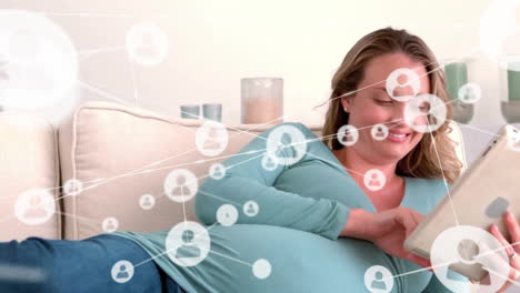 Animation-of-network-of-connections-with-icons-over-pregnant-caucasian-woman-using-tablet