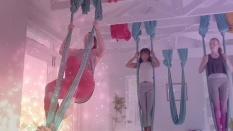 Animation-of-glowing-particles-over-diverse-female-instructor-and-teenagers-practicing-aerial-yoga