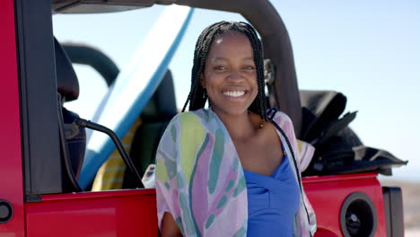 Young-African-American-woman-smiles-beside-a-red-vehicle-on-a-road-trip