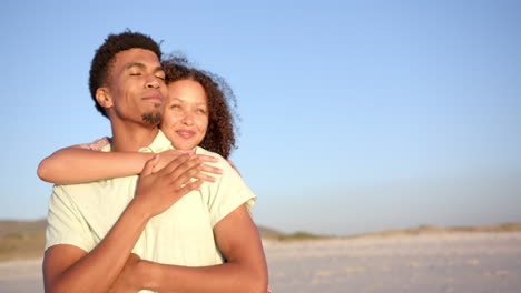 Biracial-couple-embraces-on-a-sandy-beach-at-daytime-with-copy-space