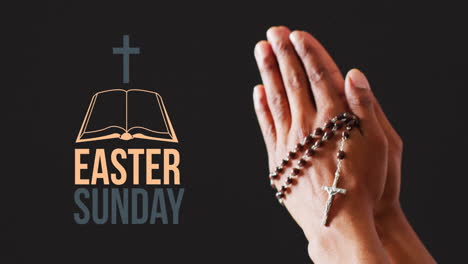 Animation-of-easter-sunday-text-over-biracial-woman's-praying-hands-with-rosary-on-black-background