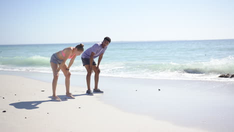 Young-Caucasian-woman-and-biracial-man-are-exercising-on-a-sunny-beach-with-copy-space