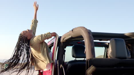 Young-African-American-woman-enjoys-a-sunny-day-at-the-beach-with-her-car-on-a-road-trip