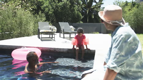 Biracial-family-enjoys-a-sunny-day-by-the-pool,-with-a-child-ready-to-jump-in