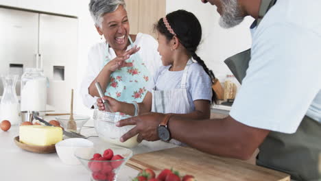 Biracial-grandparents-are-baking-with-a-young-girl,-all-smiling-in-a-bright-kitchen