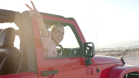 Young-Caucasian-woman-enjoys-a-sunny-beach-drive-in-a-red-jeep-on-a-road-trip