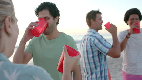 Young-Caucasian-woman-and-diverse-group-of-men-enjoy-drinks-on-the-beach-at-a-party