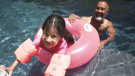 A-biracial-girl-with-arm-floaties-enjoys-pool-time-with-her-grandfather