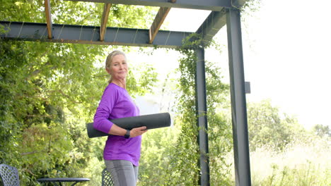 Senior-Caucasian-woman-holds-a-yoga-mat-outdoors,-with-copy-space