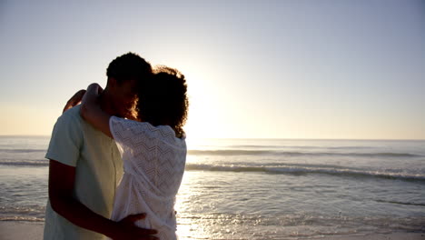 Biracial-couple-embraces-lovingly-on-a-beach-at-sunset-with-copy-space
